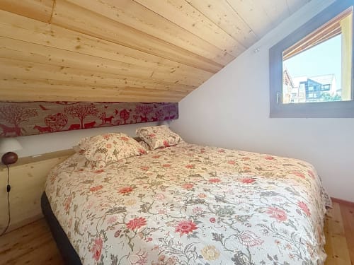 Chambre douillette sous les combles aux Tanières de Montgenèvre avec poutres en bois, literie fleurie et vue montagne