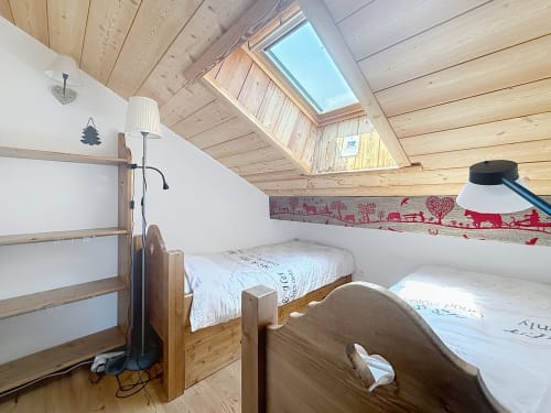 Chambre mansardée aux Tanières de Montgenèvre avec deux lits en bois, lucarne, poutres apparentes et vue montagne