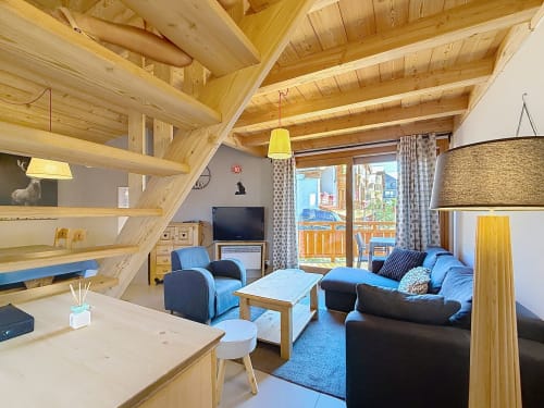 Lumineux séjour duplex en bois à Montgenèvre avec poutres apparentes, sièges bleus, vue sur balcon et paysage montagnard