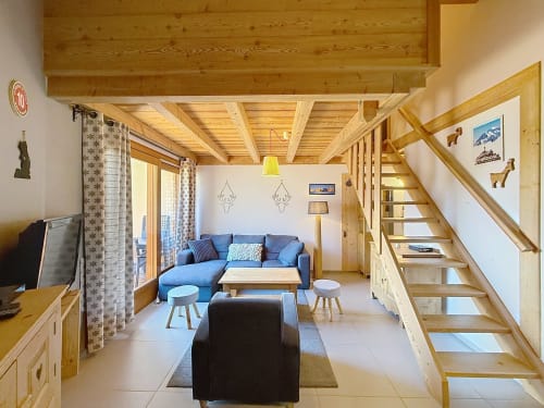 Séjour lumineux en bois avec canapé bleu, escalier et vue sur les montagnes, appartement de Montgenèvre