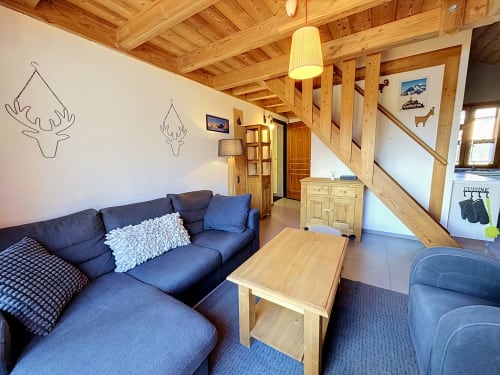 Canapé bleu et table bois dans un salon moderne aux poutres apparentes du duplex Les Tanières de Montgenèvre