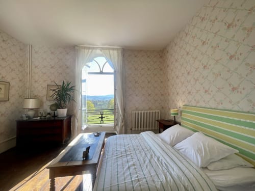 Chambre lumineuse au Château de Vaux Morvan avec tête de lit à rayures vertes, vue sur la campagne depuis le balcon, papier peint fleuri