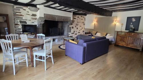 Grand salon du Manoir de la Bégaudière avec cheminée, canapé violet, table à manger et poutres en bois