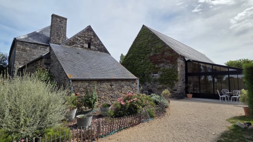 Manoir de la Bégaudière en pierre à Mont-Dol, murs couverts de lierre, fleurs du jardin et terrasse vitrée moderne