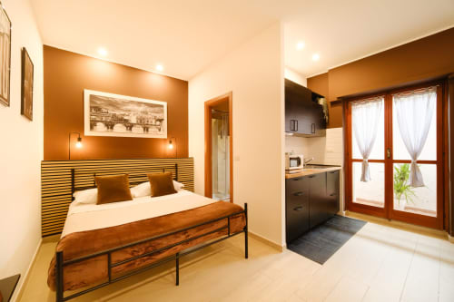 Loft camera da letto St Peter 83 con parete accent arancione, letto in legno, angolo cottura e porta balcone a Roma