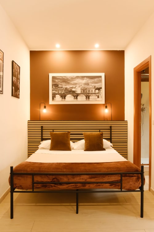 Camera da letto calda in toni arancioni con testata a righe, biancheria bianca e arte con veduta di Roma presso M&D RomeVacation