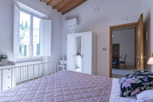 Camera da letto luminosa con letto trapuntato, armadio bianco, travi in legno e vista sulla città a Firenze