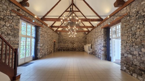 Élégante salle d'événements en pierre du Manoir de la Bégaudière à Mont-Dol avec poutres bois, lustre et grandes fenêtres