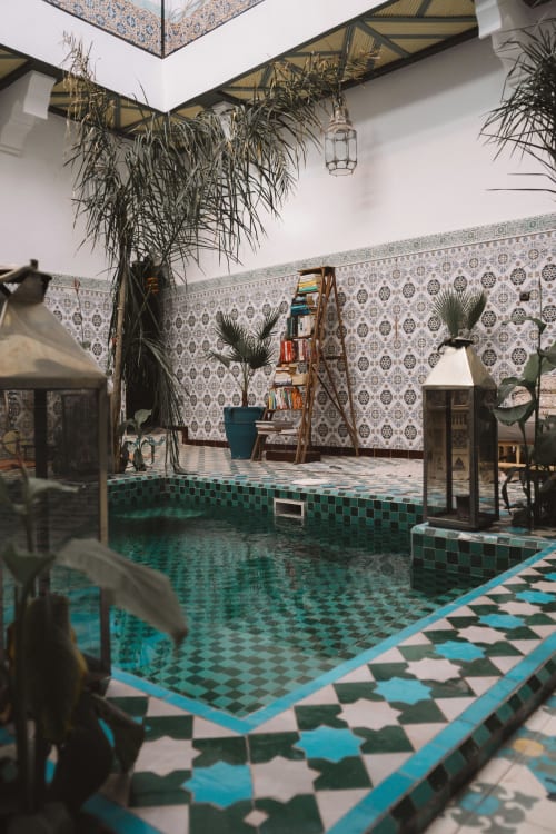 Cour de riad marocain avec zelliges turquoise, bassin central, plantes suspendues et papiers peints à motifs chez Eucalyptus