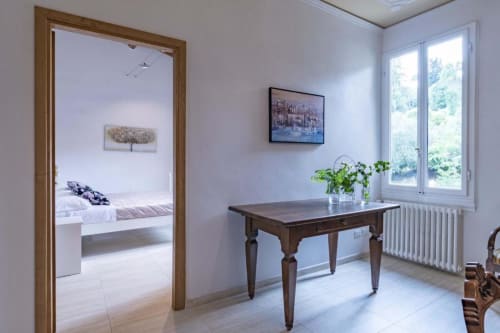 Luminoso spazio di lavoro fiorentino con tavolo in legno, piante e vista sulla città attraverso le porte vetrate verso la camera da letto