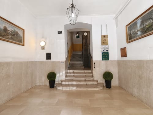 Elegante vestíbulo del Hotel Príncipe Amedeo con escalera de mármol, lámpara colgante clásica y cuadros decorativos enmarcados.