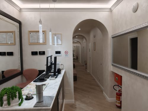 Mostrador de recepción del Hotel Príncipe Amedeo con ordenador, pasillo con arco y elegante diseño interior en tonos beige