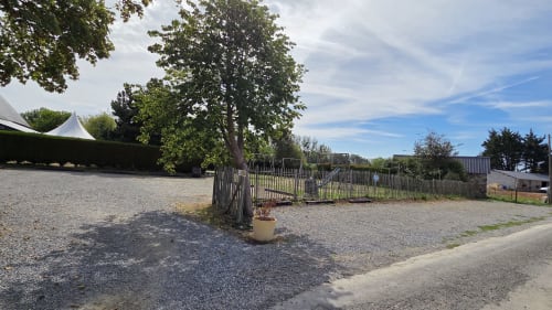 Cour gravillonnée du Manoir de la Bégaudière à Mont-Dol avec portail en bois, arbre majestueux et charme rustique