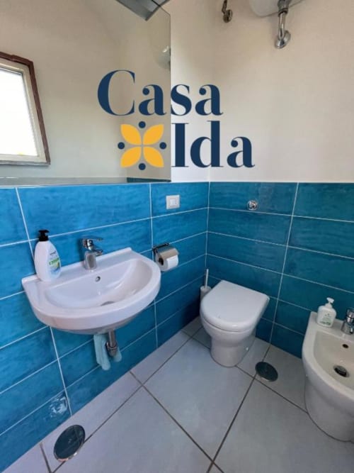 Bagno di Casa Ida con piastrelle blu, lavabo bianco, toilette e bidet nell'appartamento Vietri