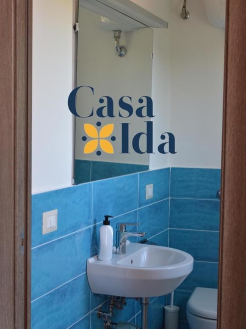 Bagno di Casa Ida a Vietri con piastrelle azzurre, lavabo rotondo bianco e specchio del brand in questo appartamento B&B italiano