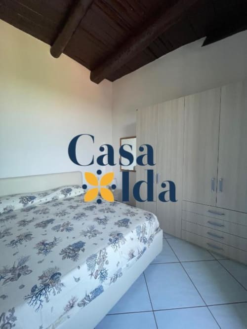 Camera da letto di Casa Ida a Vietri con letto a motivi blu, armadio bianco, travi in legno a vista e pavimento in piastrelle.