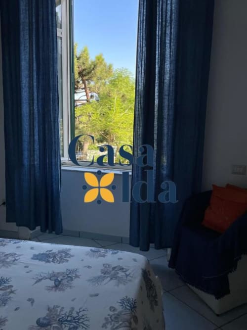 Camera da letto dell'appartamento Casa Ida con vista mare, tende blu e alberi costieri visibili da finestra a Vietri