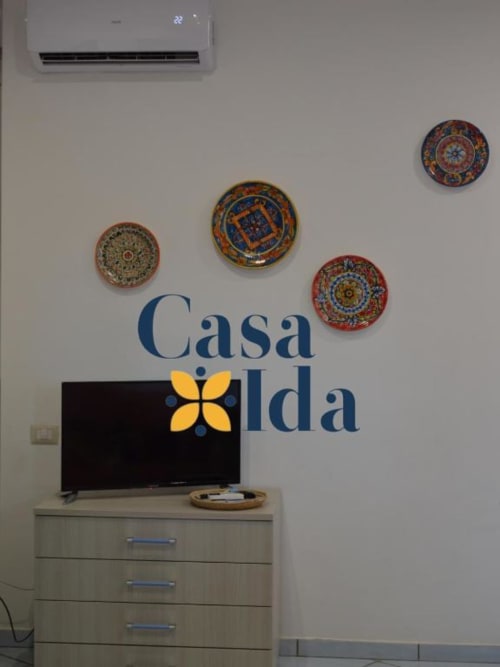 Interno dell'appartamento Casa Ida con piatti decorativi a muro, TV a schermo piatto su mobile in legno e climatizzatore