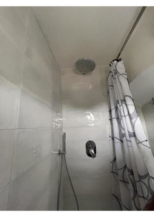 Moderna cabina doccia con soffione pioggia overhead e doccetta manuale, piastrelle subway bianche e tenda a righe