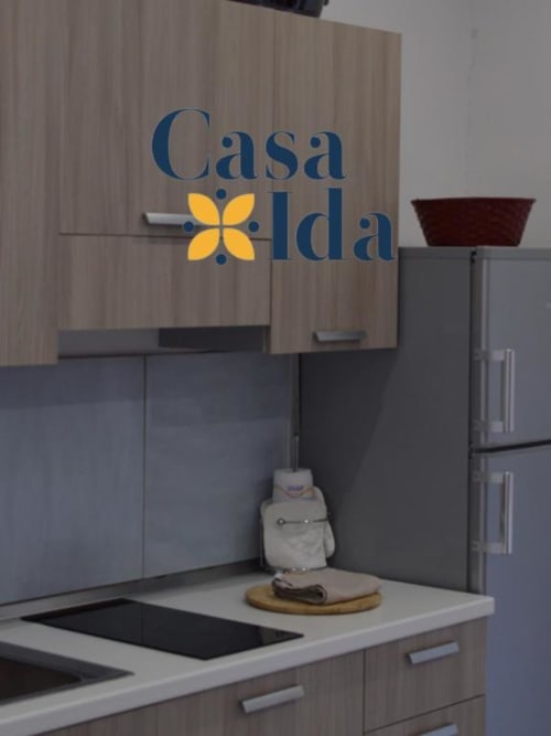 Cucina di Casa Ida con logo blu, fornello, frigorifero e una civetta decorativa sul piano cottura nell'appartamento di Vietri