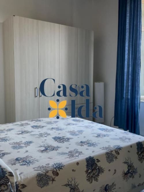 Camera da letto Casa Ida a Vietri con biancheria floreale, armadio, tende blu e branding appartamento vista mare