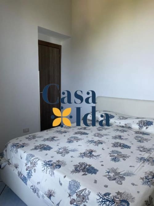 Camera da letto di Casa Ida a Vietri con biancheria blu floreale, porta in legno scuro e vista sul mare