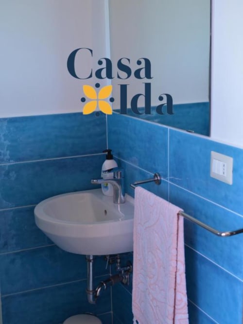 Bagno di Casa Ida a Vietri con piastrelle blu, lavabo bianco rotondo e asciugamano rosa