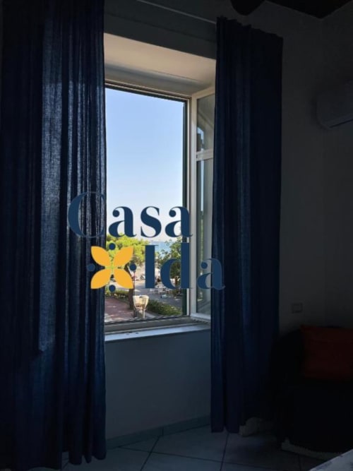 Ingresso di Casa Ida a Vietri con vista sul mare, tende scure incorniciano la porta vetrata che si apre sulla terrazza costiera