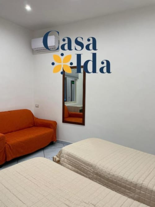 Camera da letto dell'appartamento Casa Ida a Vietri con due letti singoli, divano arancione, specchio e climatizzatore