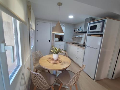 Moderna sala de estar-cocina en apartamento Casa El Abuelo, Bronchales, con mesa redonda de madera, electrodomésticos blancos y luminarias colgantes