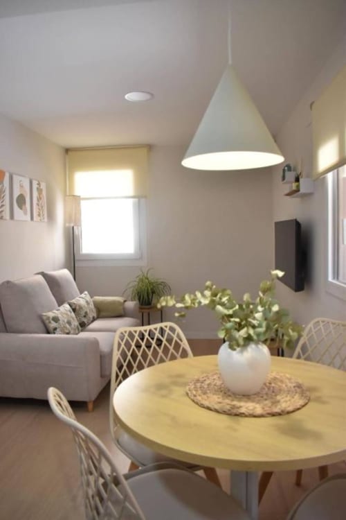 Sala de estar y comedor moderno con mesa redonda de madera, sofá gris, lámpara colgante y plantas en el apartamento Casa El Abuelo