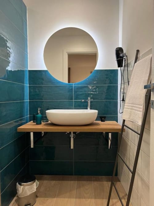 Bagno moderno a Casa Ida a Vietri con piastrelle turchesi, specchio rotondo illuminato, lavabo bianco su mobile in legno