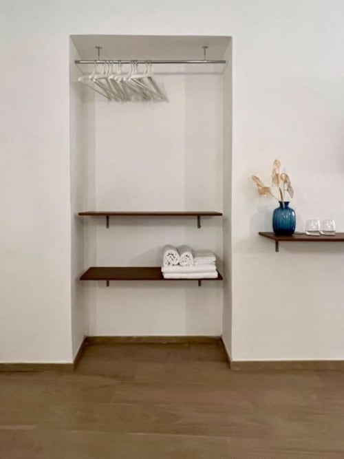 Moderno ripostiglio a Casa Ida con scaffali in legno, asta appendiabiti con grucce bianche, asciugamani arrotolati e vaso blu con fiori secchi
