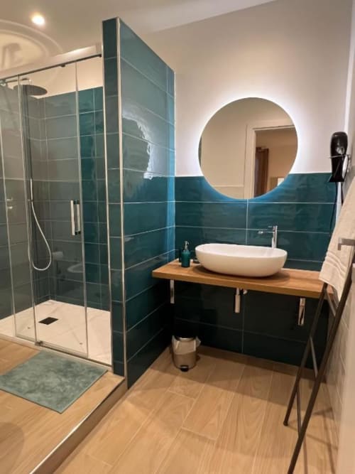 Bagno moderno a Casa Ida a Vietri con piastrelle azzurre, specchio rotondo, mobile vanità in legno e doccia con box in vetro