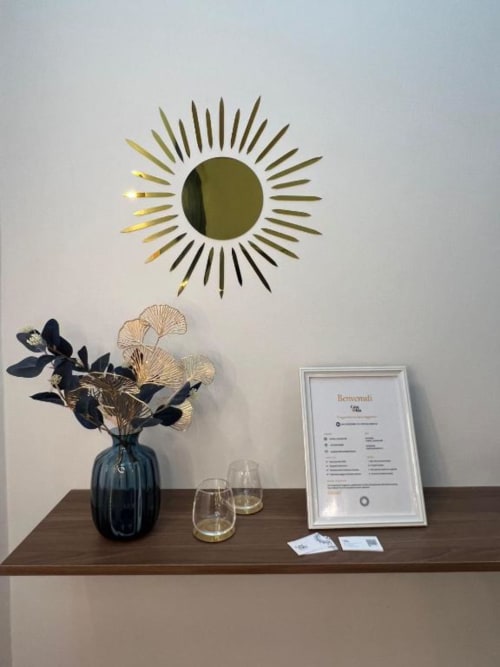 Elegante ingresso di Casa Ida Vietri con specchio sole, vaso scuro con fiori secchi, cartello benvenuto e design moderno