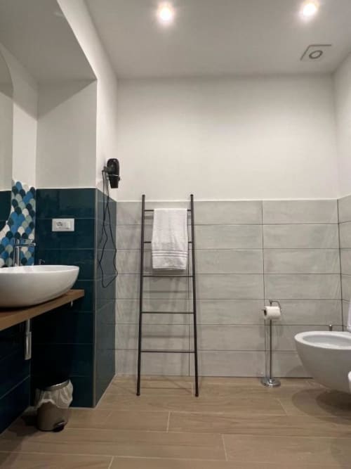 Bagno moderno della Deluxe Room di Casa Ida a Vietri con doppio lavabo, piastrelle blu teal scuro, scaletta portasciugamani e pavimento in legno