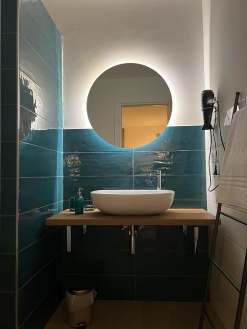 Bagno moderno a Casa Ida a Vietri con specchio circolare illuminato, lavabo bianco, piastrelle turchesi e mobiletto in legno