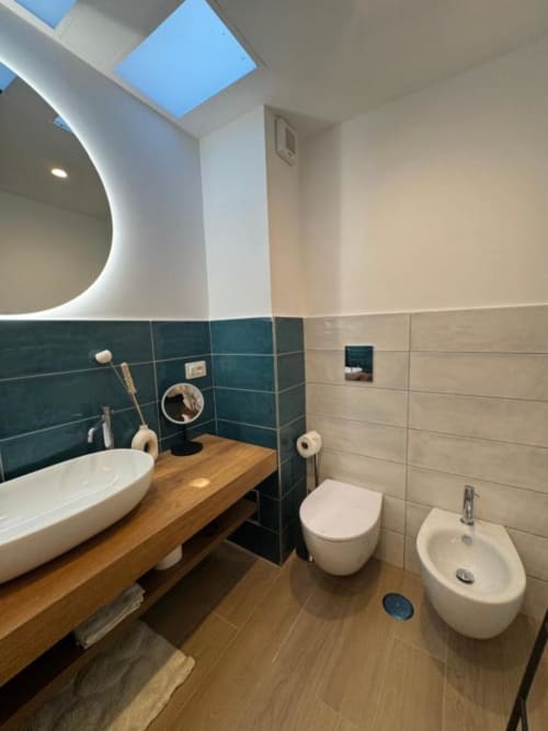 Bagno moderno a Casa Ida a Vietri con rivestimenti in piastrelle turchesi, mobile in legno, toilette a muro, bidet e lucernario