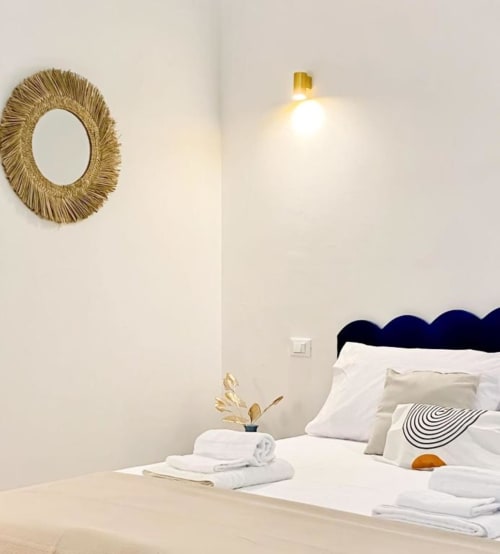 Camera Deluxe moderna Casa Ida a Vietri con specchio dorato a raggiera, biancheria bianca, testata blu navy e design ricercato