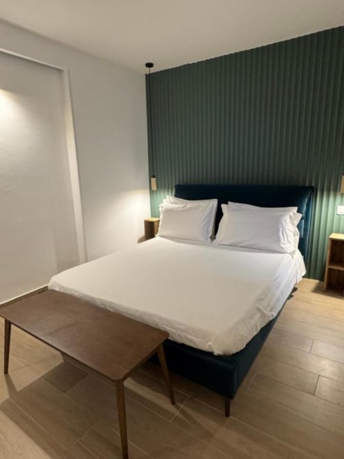 Camera moderna di Casa Ida Vietri con letto nero, biancheria bianca, tende verdi, panca in legno e pavimento piastrellato