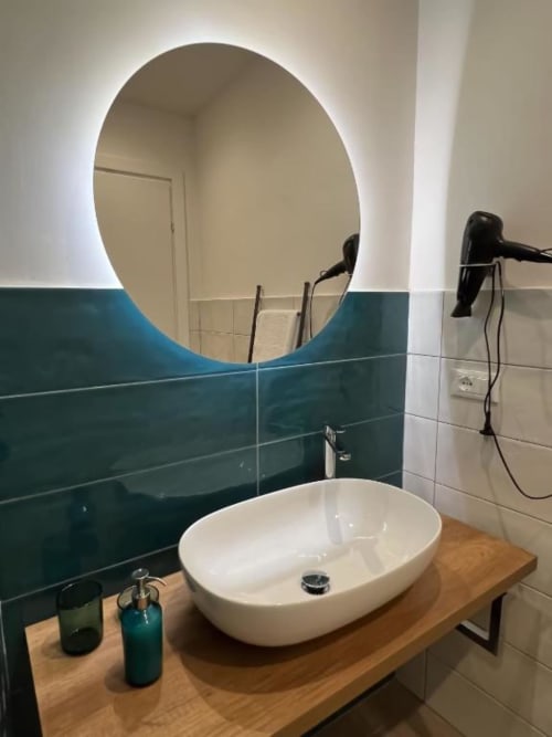 Bagno moderno a Casa Ida a Vietri con specchio rotondo illuminato, lavabo bianco su mobile in legno e piastrelle teal