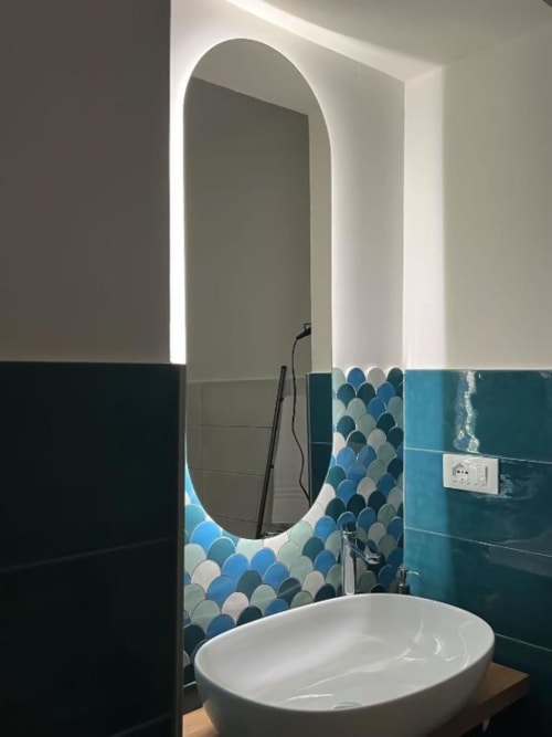 Bagno moderno di Casa Ida a Vietri con specchio ovale illuminato, piastrelle bianche e blu a squame di pesce, e lavabo bianco sospeso.