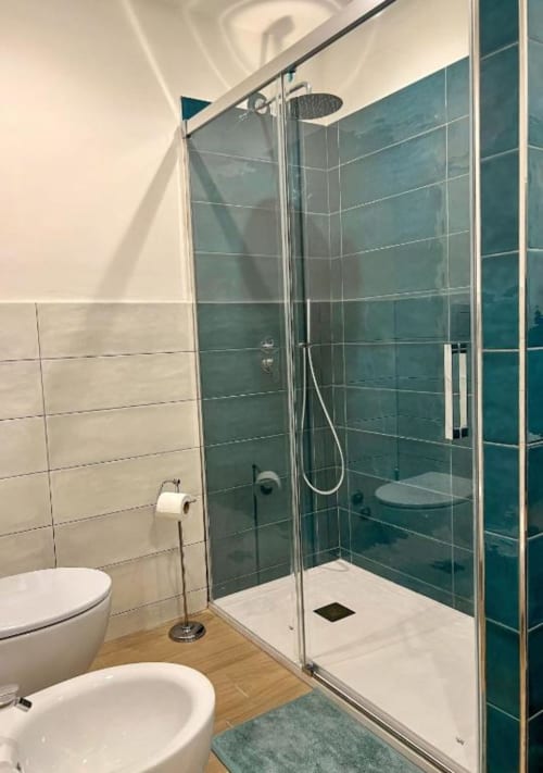 Bagno moderno con doccia rivestita in piastrelle turchesi, sanitari bianchi e pavimento in legno presso Casa Ida a Vietri, Italia