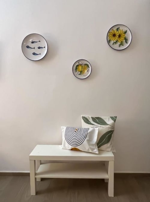 Panca bianca in legno con cuscini decorativi sotto tre piatti ceramici con pesci e girasoli a Casa Ida