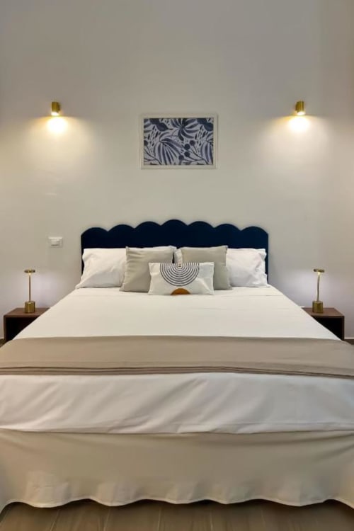 Camera moderna a Casa Ida Vietri con testata nuvola scura, biancheria bianca, applique oro e quadri botanici blu navy