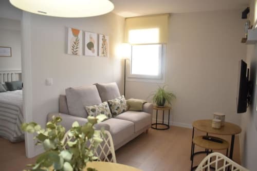 Moderno apartamento estudio en Bronchales con sofá confortable, mesa de madera, plantas y luz natural brillante desde la ventana