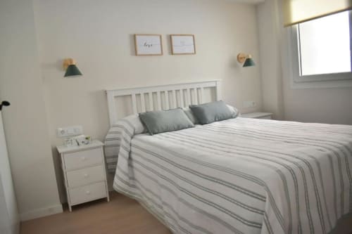 Habitación luminosa en apartamento rural Casa El Abuelo, Bronchales, con cama blanca, ropa de cama a rayas, almohadas grises y mesita de noche