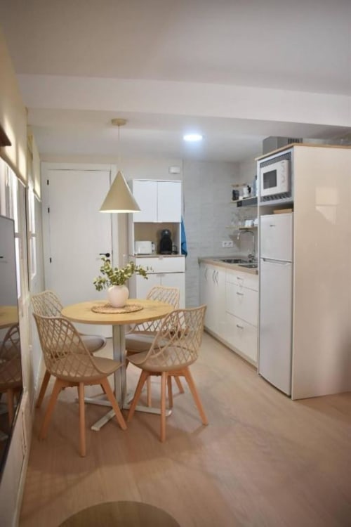 Moderna sala de estar-comedor en apartamento Casa El Abuelo, Bronchales, con mesa de madera, sillas tejidas y electrodomésticos blancos