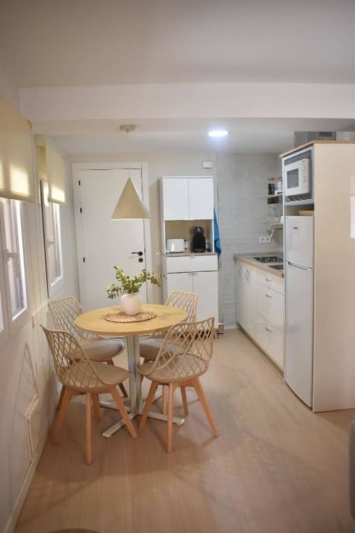 Moderna zona de cocina-comedor en el apartamento Casa El Abuelo, Bronchales, con mesa de madera, sillas tejidas y armarios blancos,