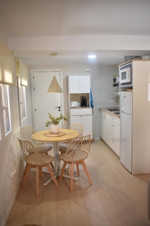 Sala comedor luminosa en apartamento Casa El Abuelo, Bronchales, con mesa redonda de madera, sillas de mimbre y acabados modernos blancos